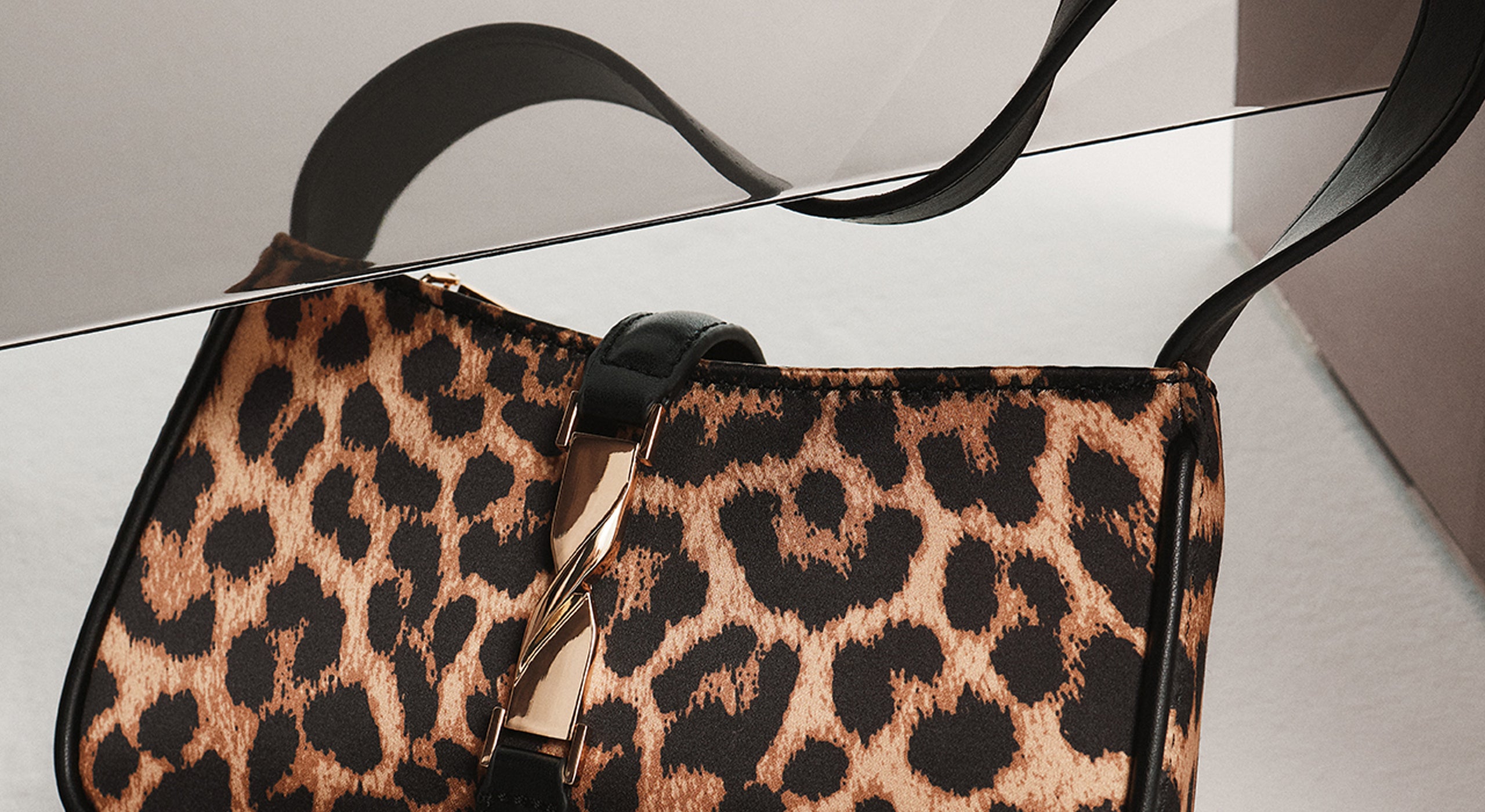 Leopard print handbag with a gold clasp on a reflective surface.