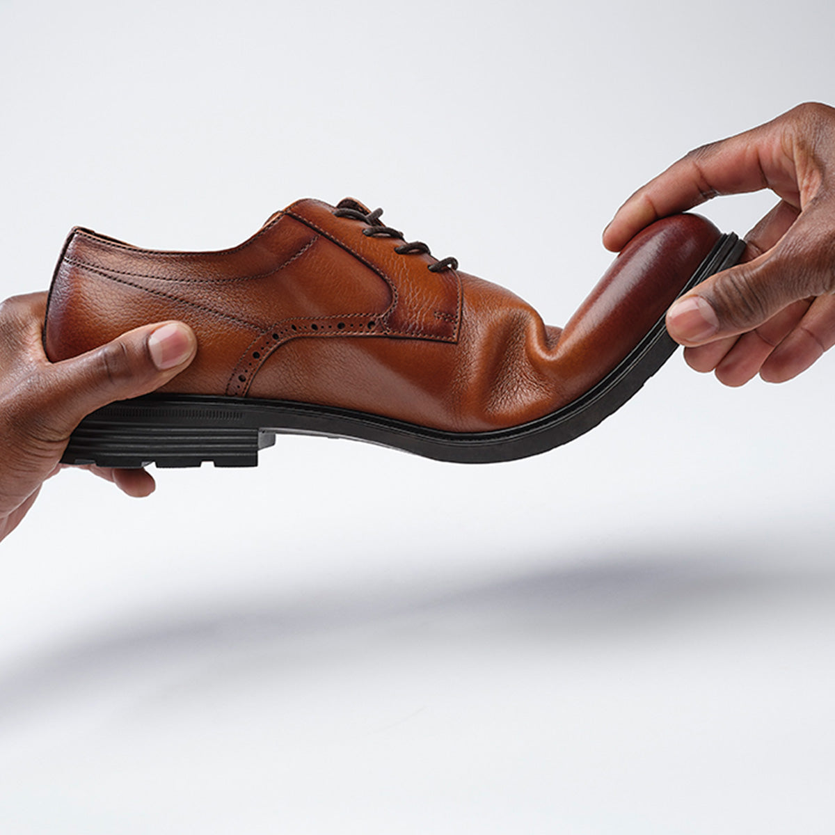 Brown leather shoe being held by two hands on a white background