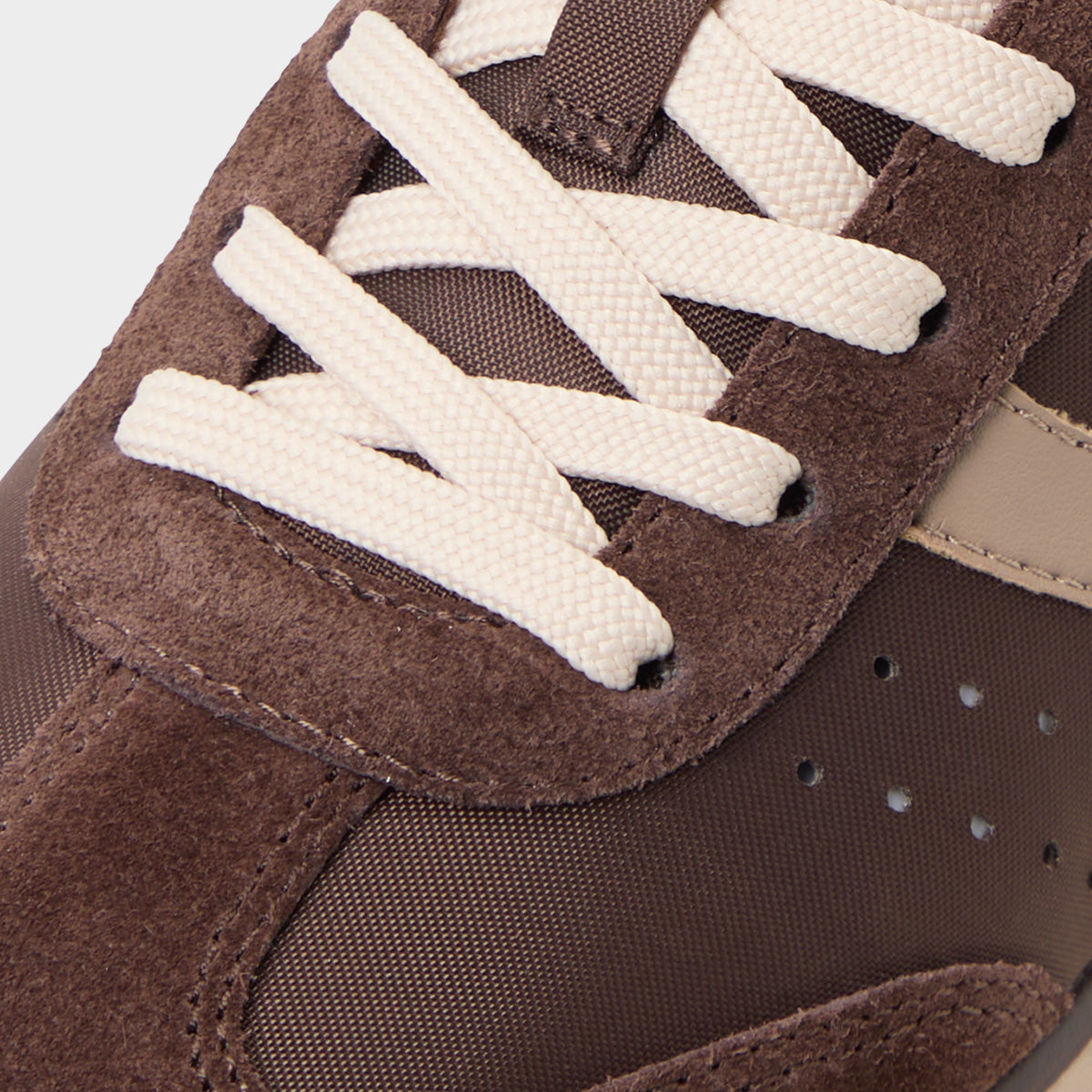Close-up of brown suede sneaker with white laces on a light gray background