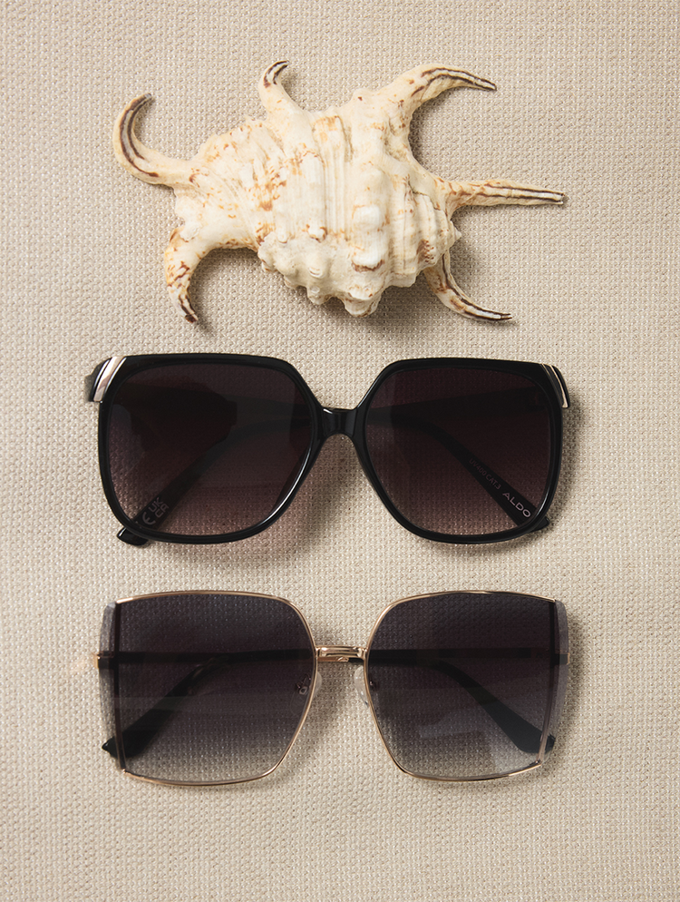 Two pairs of sunglasses with a shell on a textured beige surface.