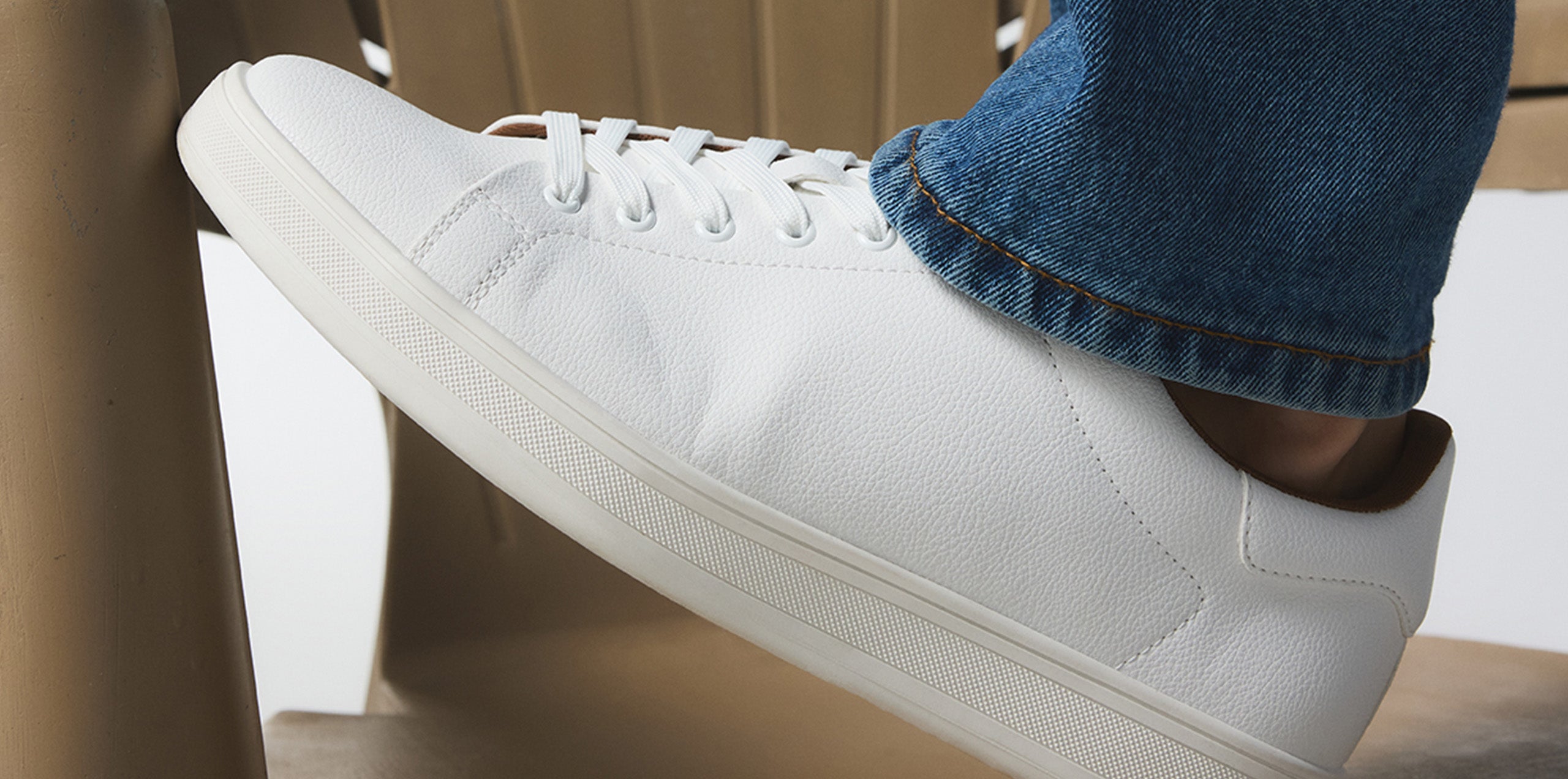 White sneaker worn with blue jeans on a brown chair.
