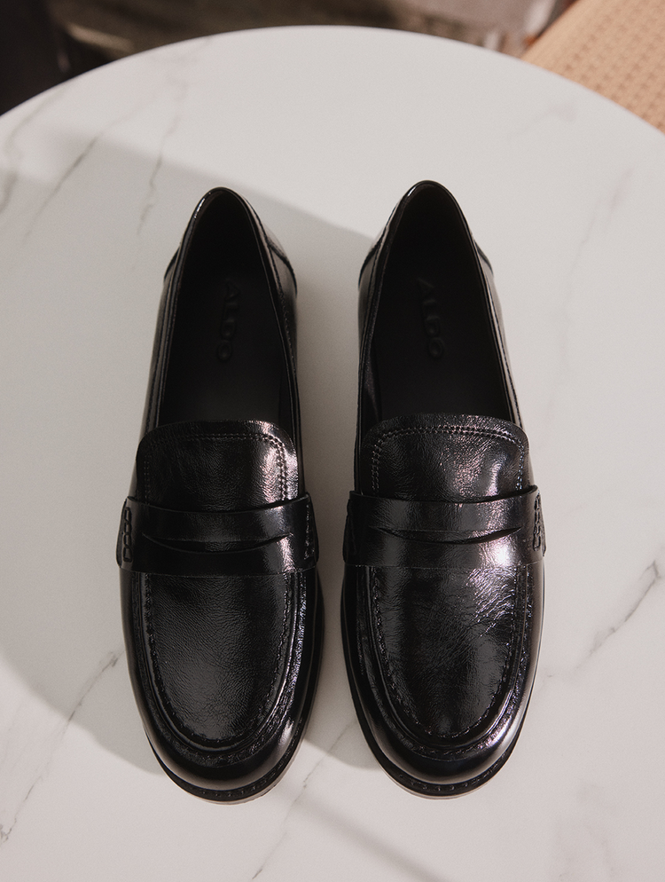 A pair of black leather penny loafers with a glossy finish, displayed on a white marble surface.